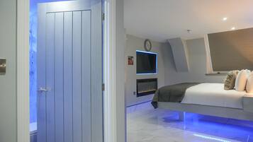 A modern bedroom with a bed, a TV mounted on the wall, and a fireplace.
