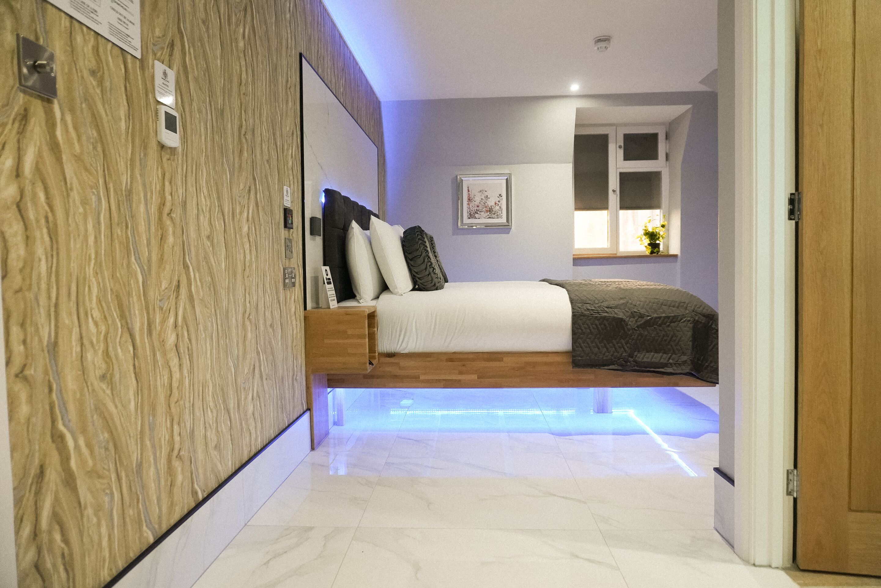 A modern bedroom with a bed, bedside table, and a wall-mounted control panel.