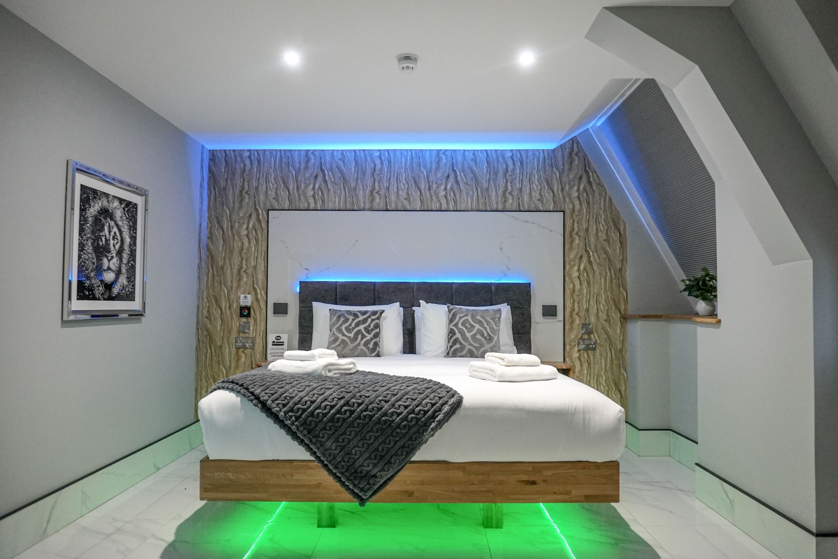 Un dormitorio moderno con cama, cabecera, una obra de arte en la pared y una lámpara en el techo.