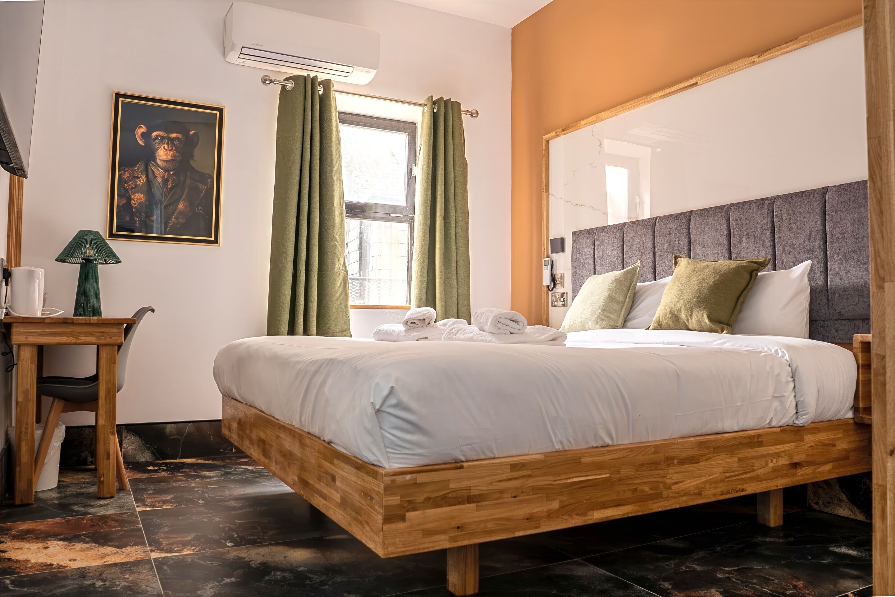 A neatly arranged bedroom with a wooden bed, a desk with a lamp, and a framed picture on the wall.