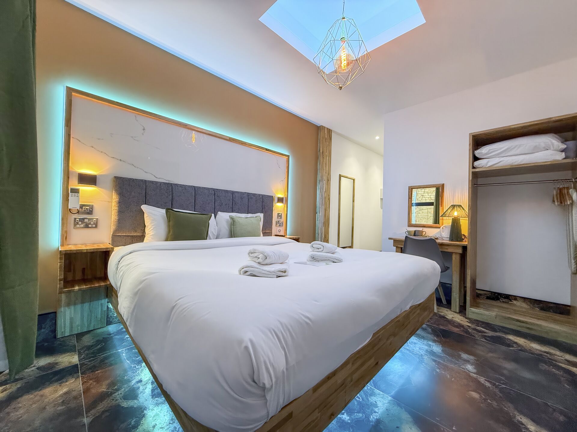 Moderni hotellihuone, jossa on suuri sänky, kattovalokuvio, puinen pääty, työpöytä lampun kanssa ja erillinen vaatehuone.
