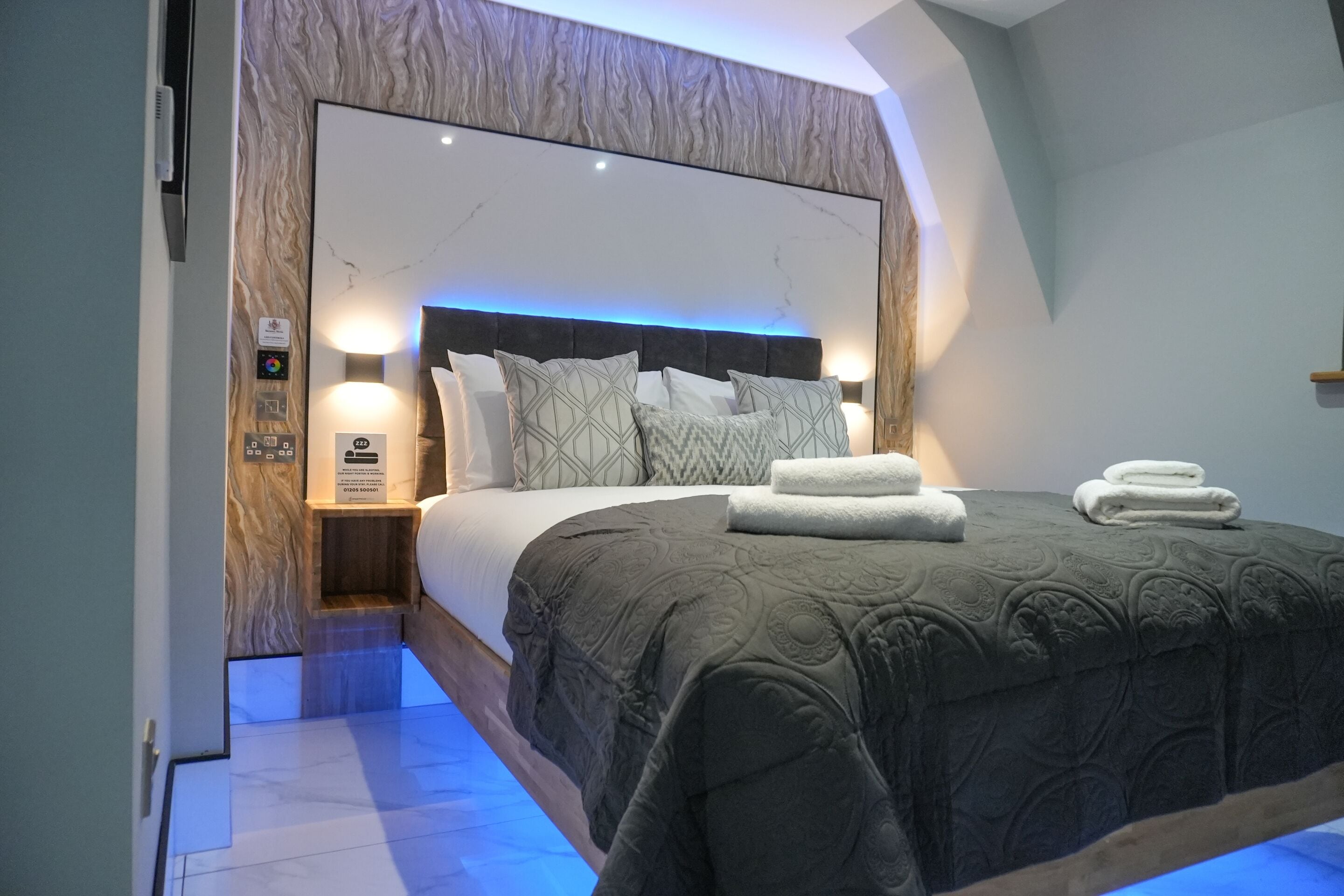 A modern bedroom with a large bed, a marble-patterned headboard, and a built-in nightstand with a lamp.