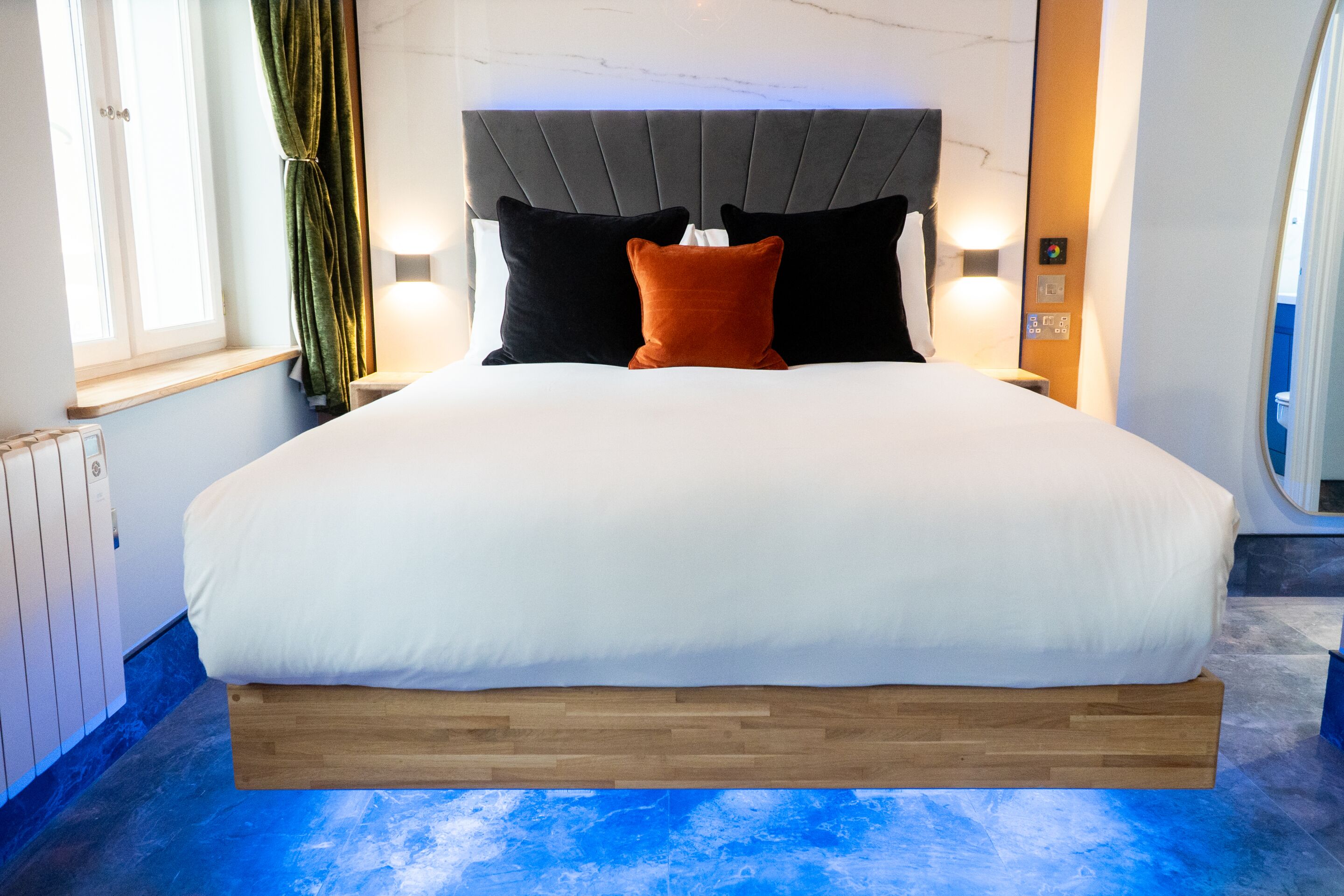 A modern hotel room with a large bed, a wooden platform, a marble headboard, and a view of the city.