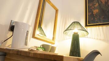 A hotel room with a wooden desk, a green lamp, a white mug, and a framed picture on the wall.