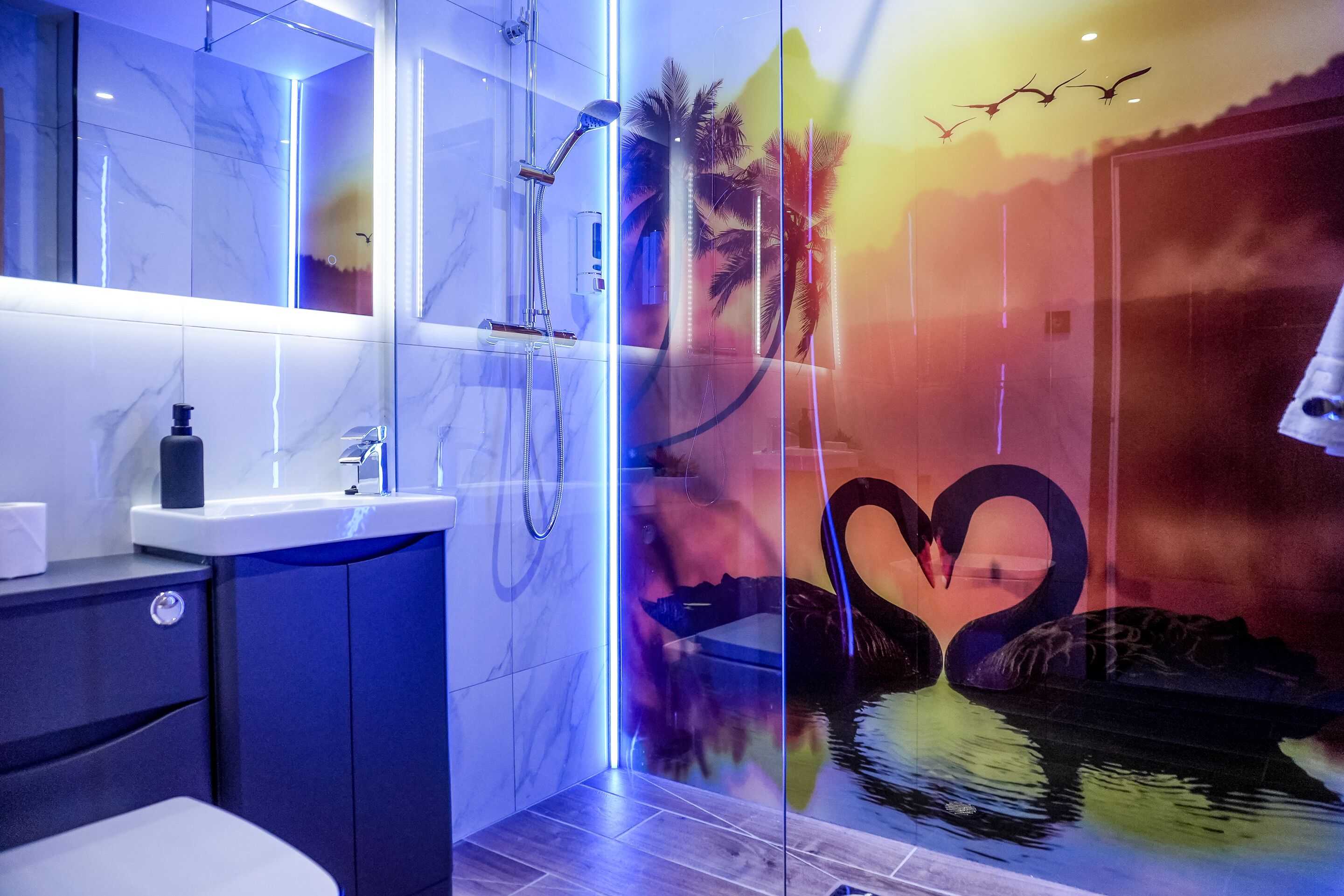 A modern bathroom with a glass shower enclosure, a marble-tiled wall, and a decorative mural of swans and palm trees.