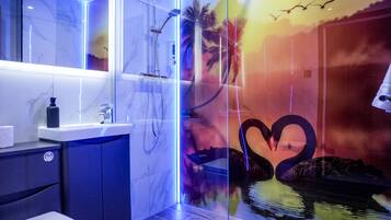 A modern bathroom with a glass shower enclosure, a marble-tiled wall, and a decorative mural of swans and palm trees.