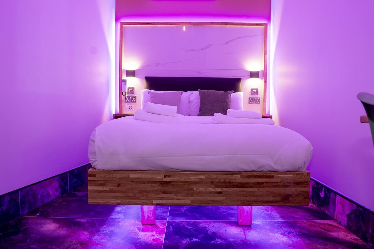 A modern bedroom with a wooden platform bed, white bedding, and purple ambient lighting.