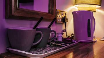 Una kitchenette con dos tazas moradas sobre una bandeja, una cafetera y una lámpara en la pared.
