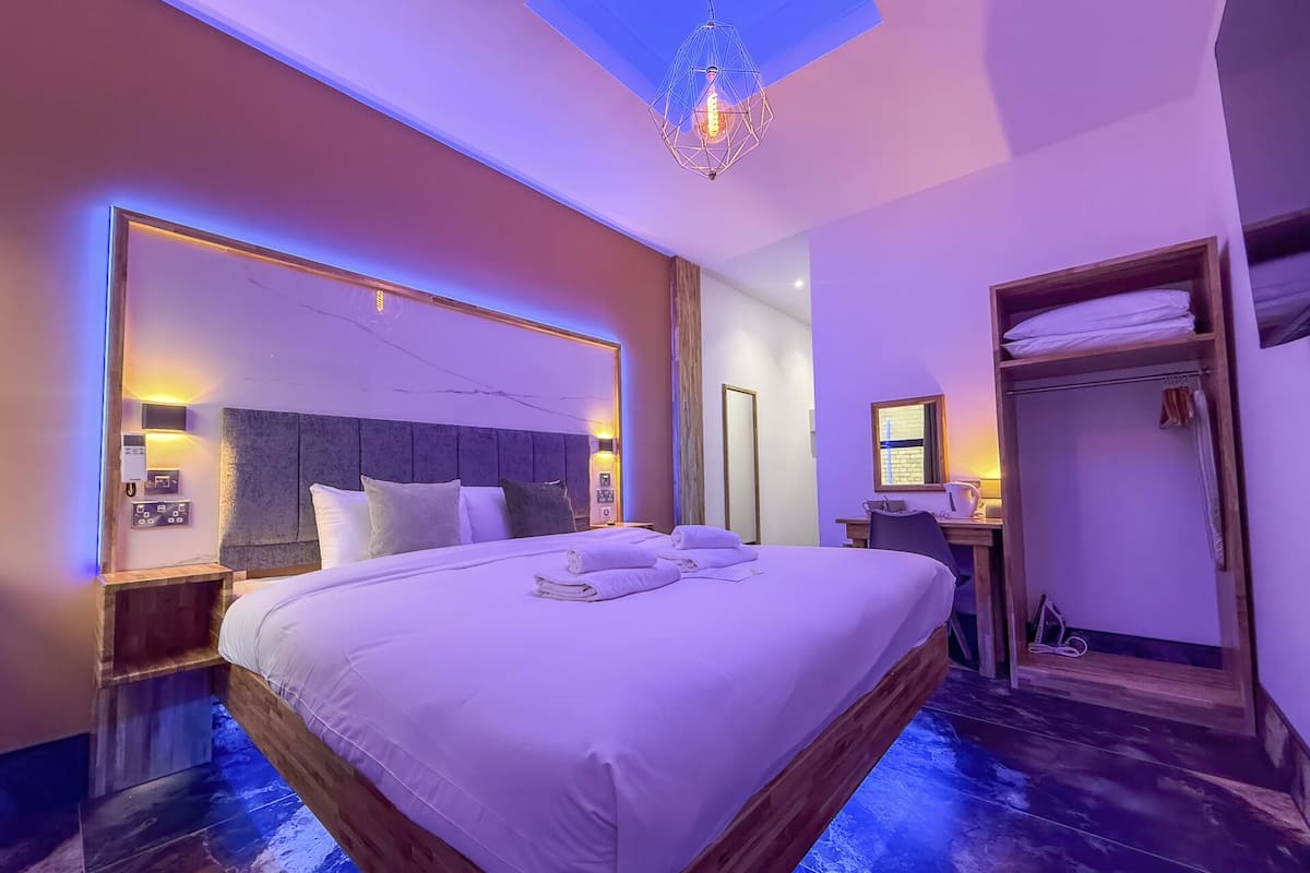 A modern hotel room with a large bed, bedside tables, a desk, and a wardrobe.