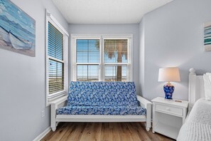 Een kamer met een blauwe gestreepte bank, een witte nachtkastje met een lamp en een bed.