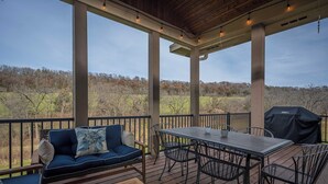 A covered outdoor deck with a sofa, table, chairs, and a grill. - Enjoy your Private 4 Acres @ Owl Creek - Hot Tub, Fire Pit (Galena)