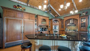 A spacious kitchen with wooden cabinets, a large island with stools, and a central range hood. - Enjoy your Private 4 Acres @ Owl Creek - Hot Tub, Fire Pit (Galena)