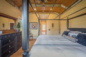 Ein Schlafzimmer mit einem großen Bett, Holzbalkendecke, einem Schminktisch und einer Tür zu einem anderen Raum.