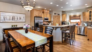 A modern kitchen with wooden cabinets, stainless steel appliances, a dining area with a wooden table and chairs, and a chandelier.