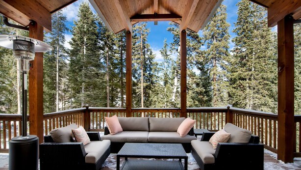 A covered deck with a sofa and coffee table, surrounded by tall trees.