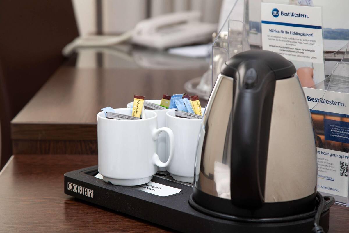 A coffee maker on a tray with two white mugs, a sign for Best Western, and a telephone on a desk.