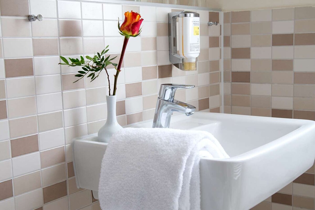 Ein Badezimmer mit einem weißen Waschbecken, einem weißen Handtuch und einer Vase mit einer Blume.