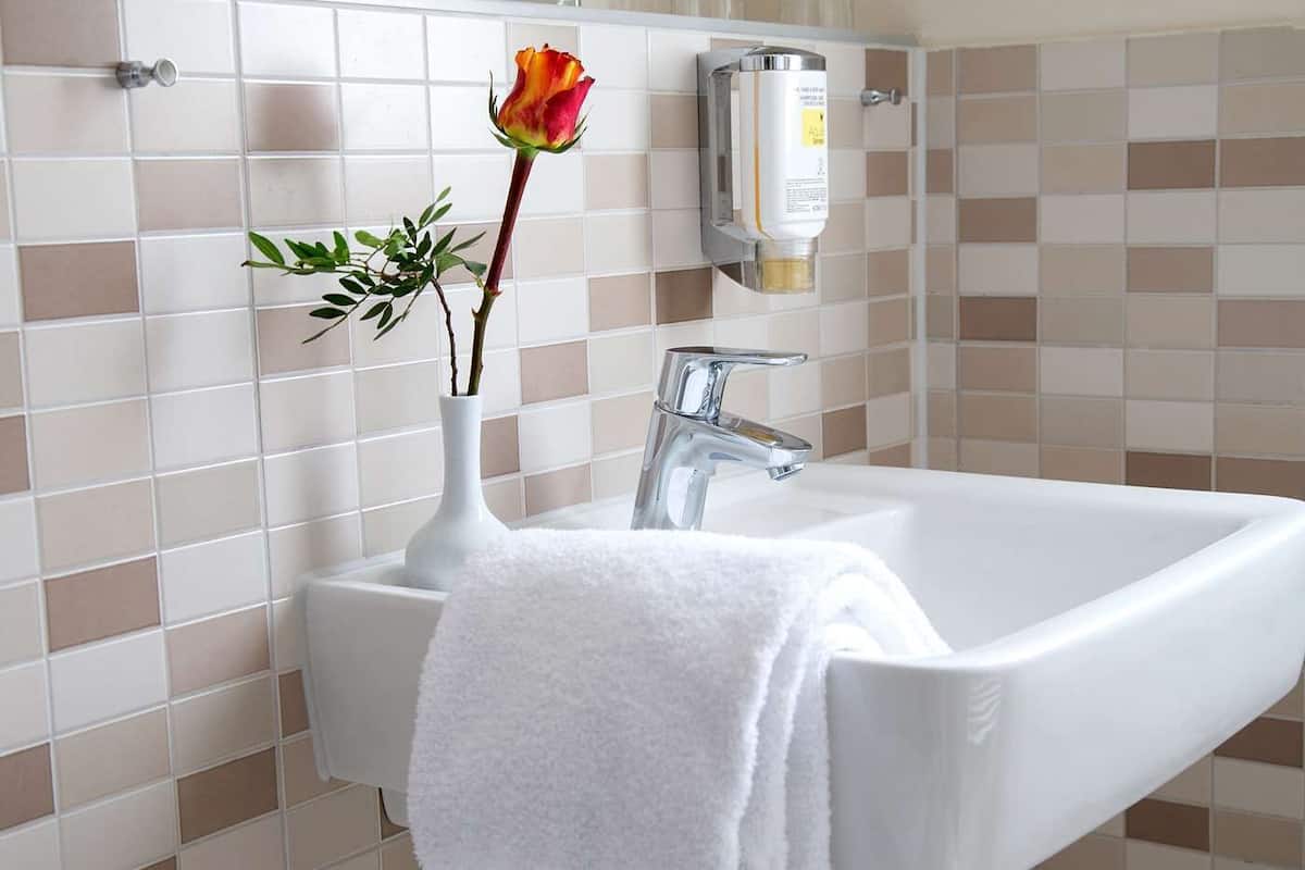 A bathroom with a white sink, a white towel, and a vase with a flower.