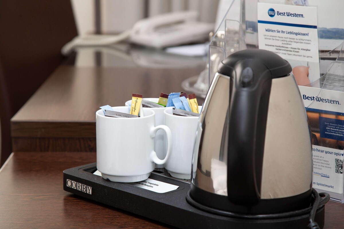 Eine Kaffeemaschine mit Auffangschale, zwei weiße Tassen und ein Best Western Schild.