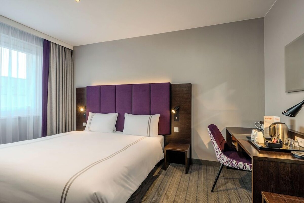 Ein Hotelzimmer mit einem großen Bett, einem Schreibtisch mit Stuhl und einem Nachttisch.