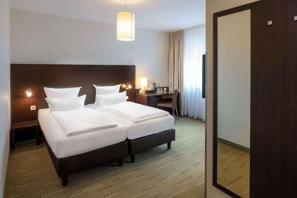 Ein Hotelzimmer mit einem großen Bett, Nachttischen, einem Schreibtisch und einem Sessel.
