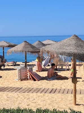 A beach with thatched umbrellas, lounge chairs, and a wooden walkway.