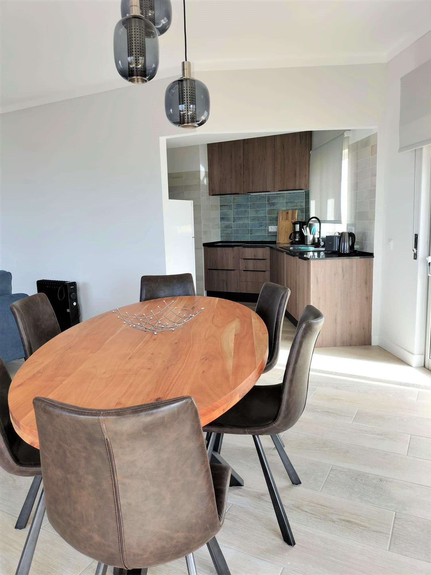 A modern dining area with a round wooden table, leather chairs, and pendant lighting.