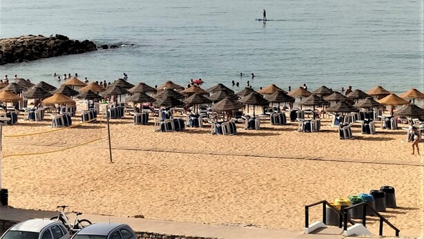 A beach with thatched umbrellas and sun loungers, a rocky breakwater, and a sailboat in the distance. - T2 Requinte A C e Vista Mar Wifi Garagem (Loulé)