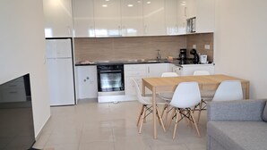 Moderni keittiö, jossa on valkoiset kaapit, sisäänrakennettu uuni sekä ruokailutila, jossa on puinen pöytä ja valkoiset tuolit.