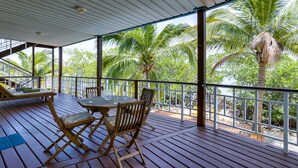 Une terrasse en bois avec une table et des chaises, offrant une vue sur un paysage tropical parsemé de palmiers.