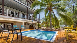 Une terrasse en bois avec une piscine, des chaises d’extérieur et un palmier.