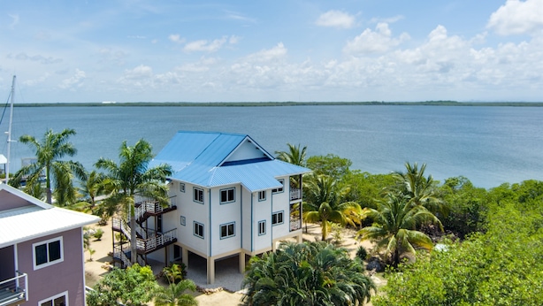 Een gebouw met twee verdiepingen, voorzien van een blauw dak, omringd door palmbomen en uitzicht op zee.
