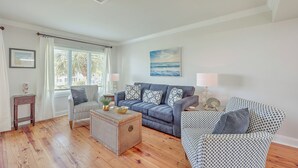 A living room with a blue sofa, patterned armchairs, a coffee table, and a window with curtains. - Port O' Call E203 - Ocean View Perfection! (Isle of Palms)