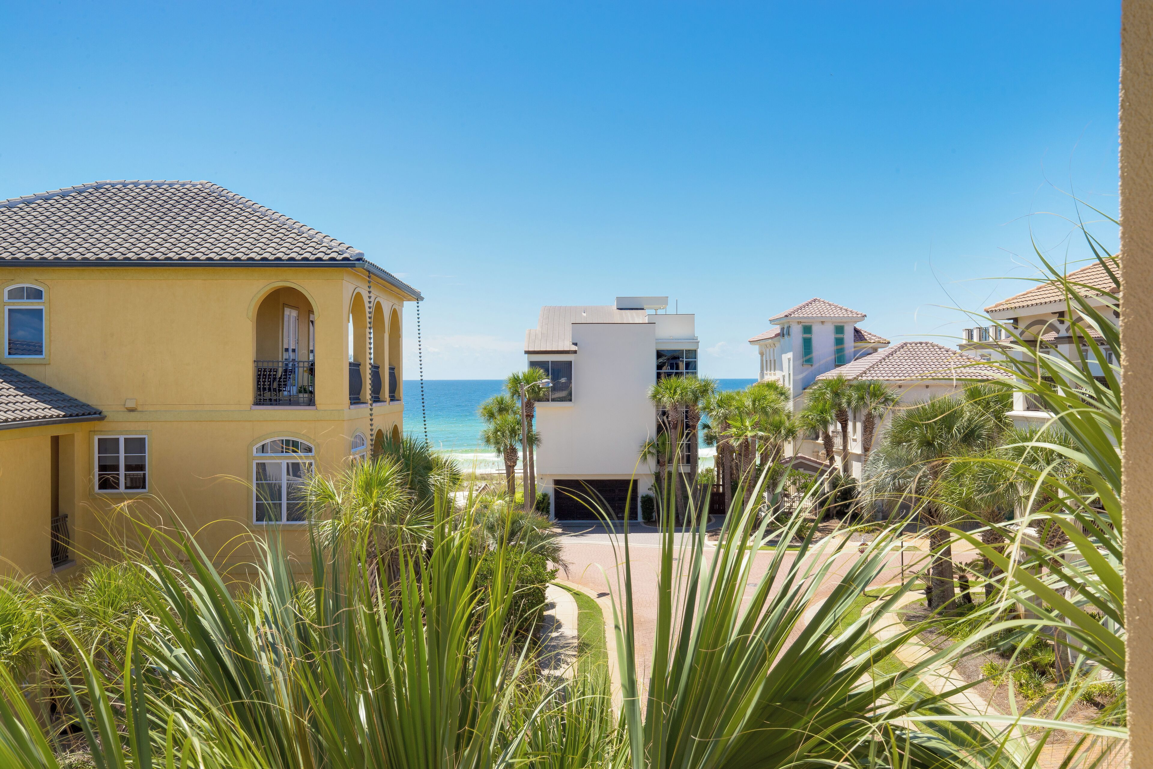 A coastal residential area with a yellow building, a white modern structure, and a beach view.