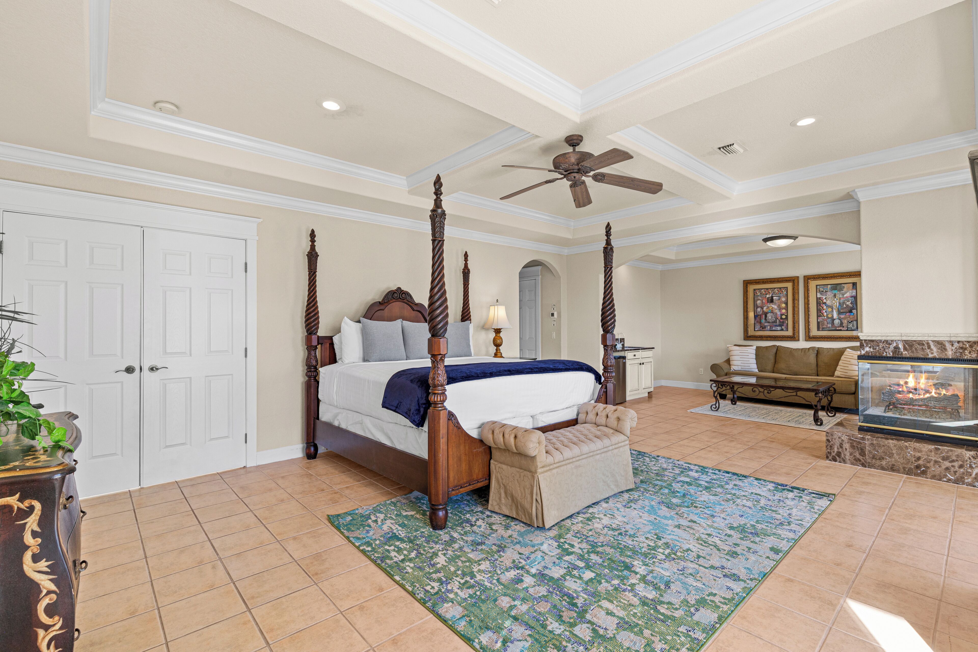 A spacious bedroom with a four-poster bed, a sitting area with a sofa, and a fireplace.
