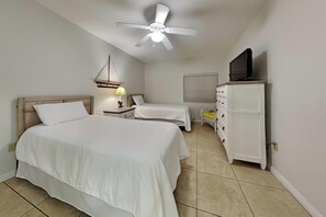A hotel room with a large bed, a smaller bed, a TV on a cabinet, a ceiling fan, and a lamp.