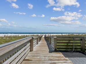 A wooden boardwalk leading to a beach with a clear sky and distant ocean view.