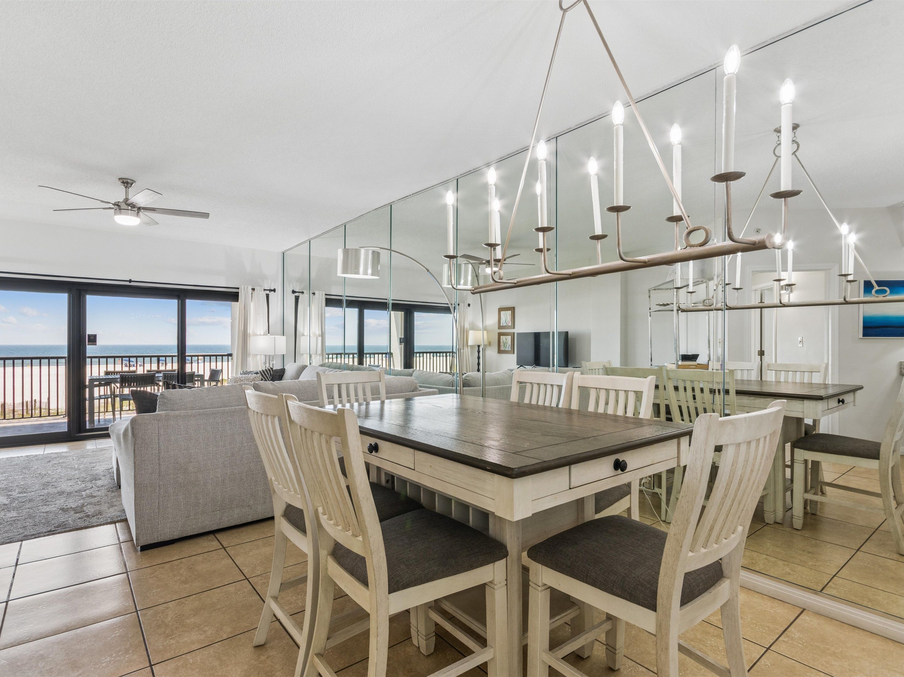 A dining area with a large table and chairs, a ceiling fan, and a view of the ocean through large windows.