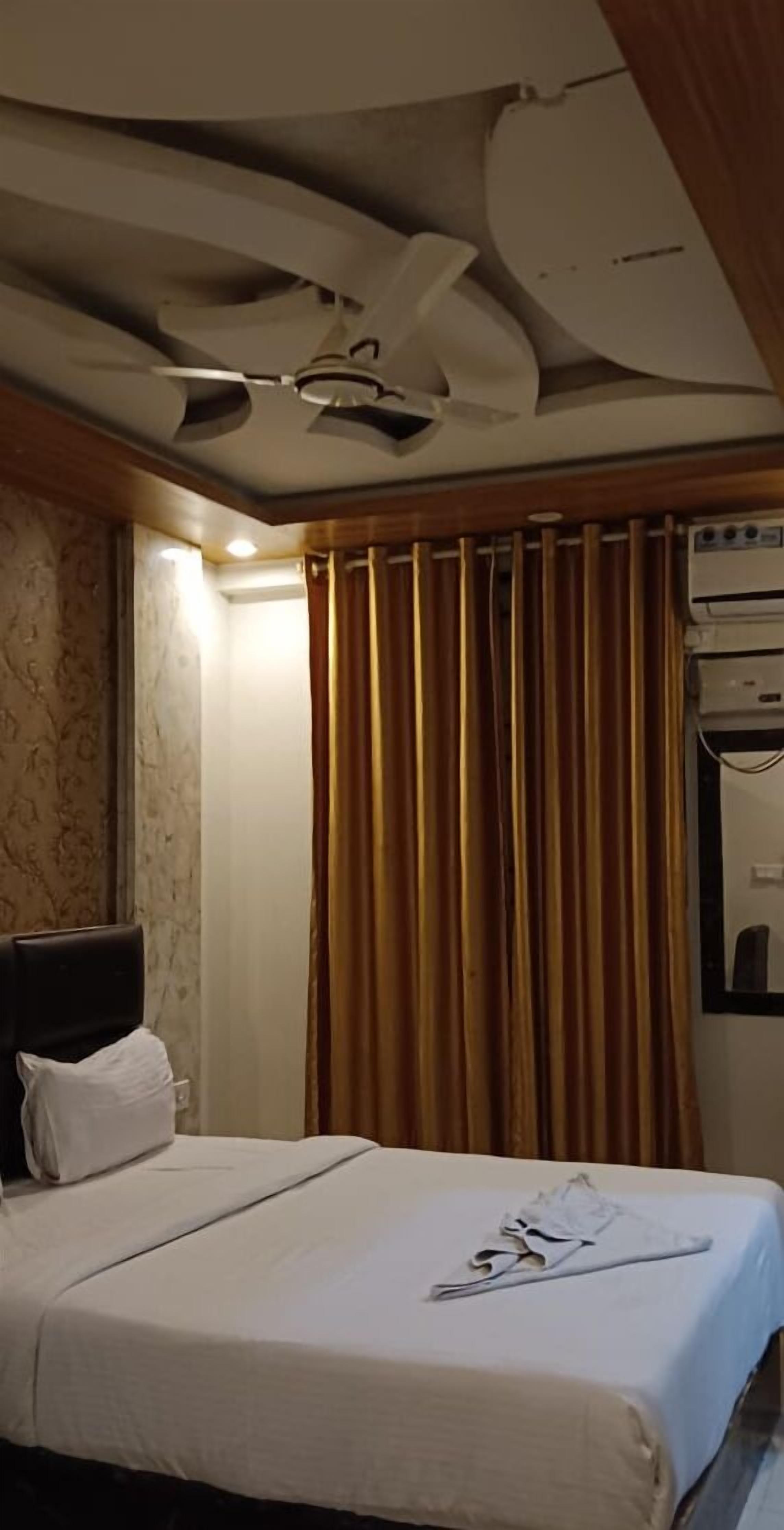 A hotel room with a bed, a ceiling fan, a wall-mounted air conditioner, and a curtain.