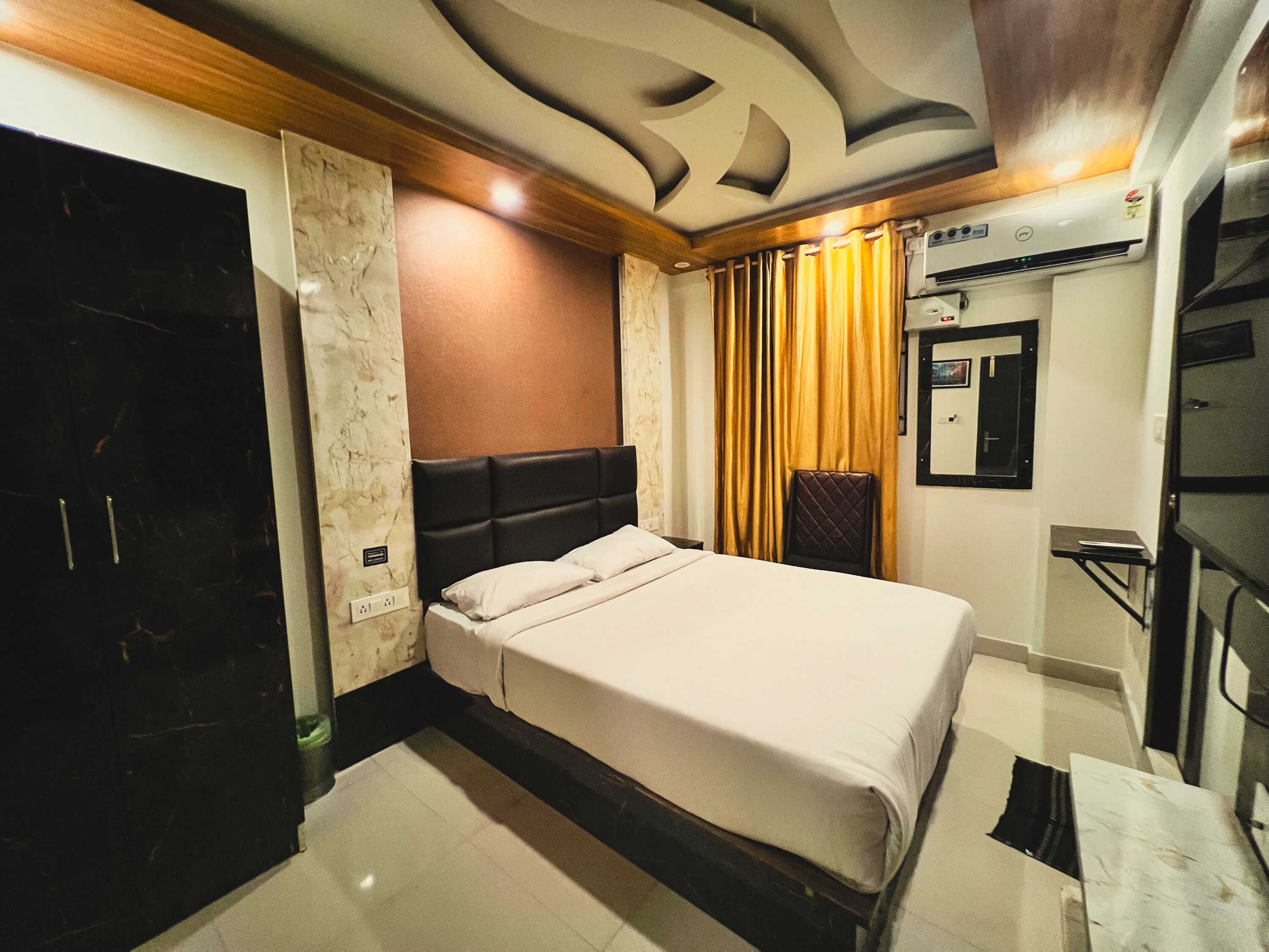 A hotel room with a bed, a wardrobe, a mirror, and a wall-mounted air conditioning unit.