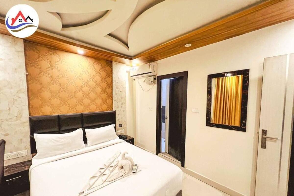 A hotel room with a bed, a nightstand, a wall-mounted air conditioner, a door with a mirror, and a window with curtains.