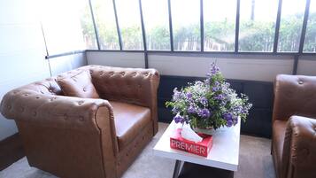 Una habitación con dos sillones de cuero marrón, una mesa blanca con una caja roja etiquetada “PREMIER” y un jarrón con flores moradas.