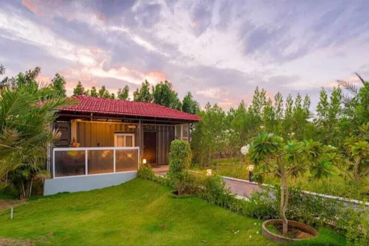Une maison moderne avec un toit rouge, entourée d’une végétation luxuriante et d’une pelouse bien entretenue.