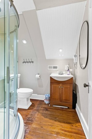 A bathroom with a glass shower enclosure, a toilet, a sink with a mirror, and wooden cabinets. - Cottage for 12, Close to Ark, Private Parking, 4BR (Williamstown)