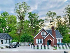 A two-story brick house with a white picket fence, a car parked in front, and trees in the background. - Cottage for 12, Close to Ark, Private Parking, 4BR (Williamstown)