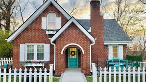 Une maison en briques avec une clôture blanche en bois, une porte verte et une guirlande accrochée à la porte d’entrée.