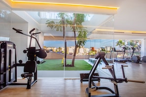 Ein modernes Fitnessstudio mit unterschiedlichen Trainingsgeräten, großen Fenstern und Blick auf eine Stadtlandschaft und Grünflächen.