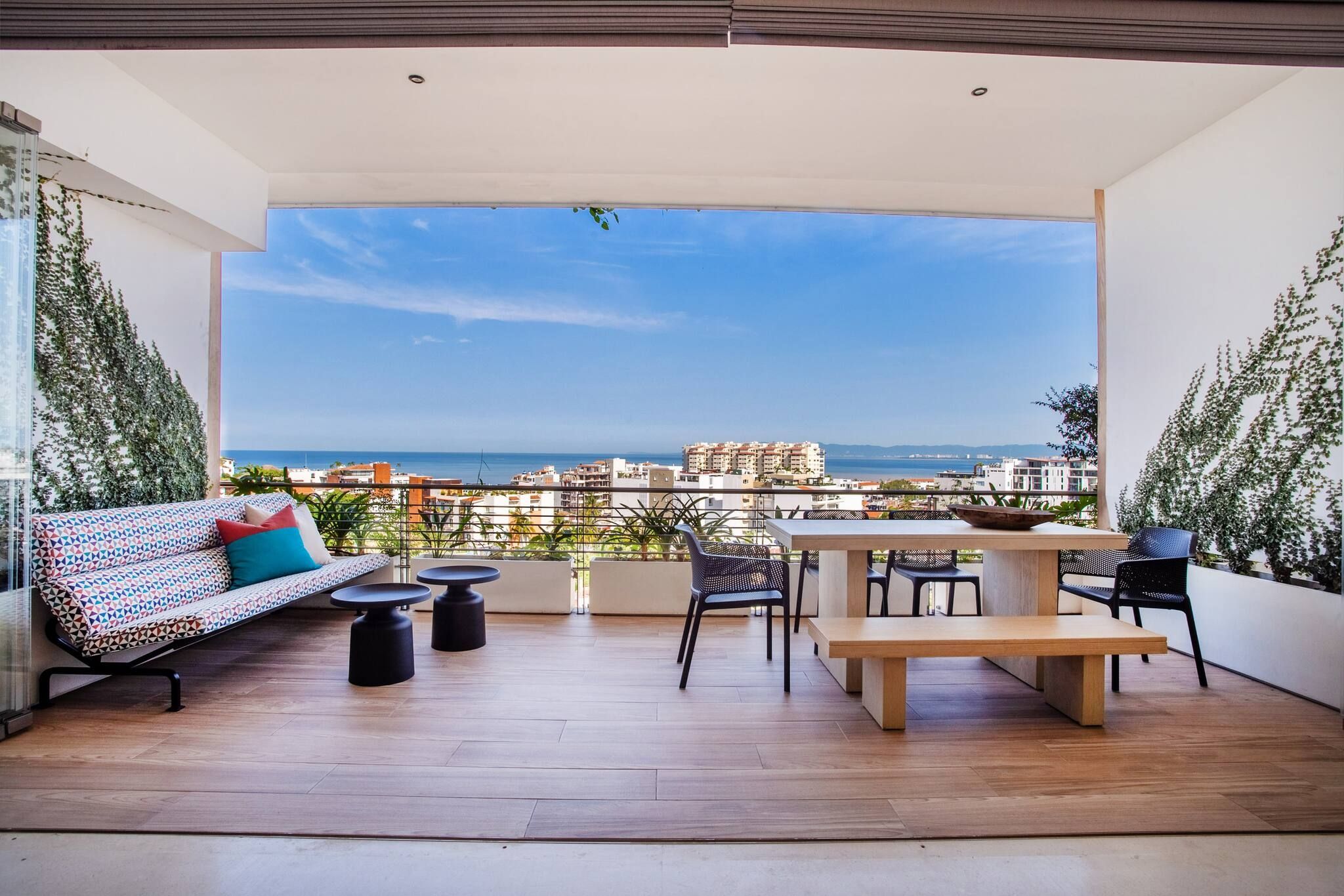 A balcony with a wooden floor, a sofa, a table, and chairs.
