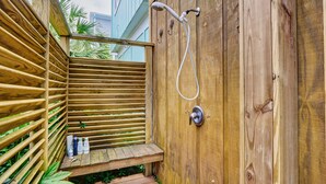 Une terrasse en bois équipée d’une douche, d’un banc et d’une petite table sur laquelle sont disposés des articles de toilette.
