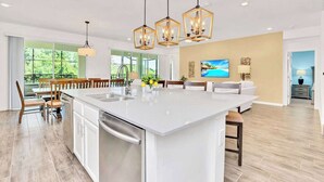 A spacious kitchen with a large island, modern pendant lights, and a view of the outdoors through large windows.